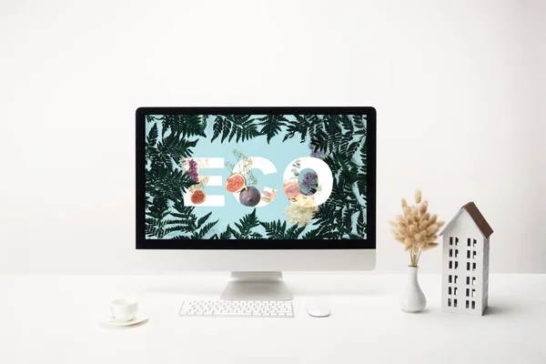 Computer with eco lettering on monitor and decoration with coffee cup on desk on white background — Stock Photo