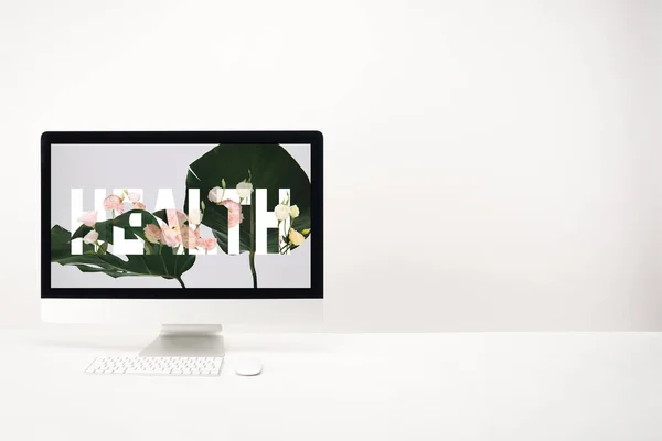 Computador com letras de saúde e folhas de monstera verdes no monitor no fundo branco — Fotografia de Stock