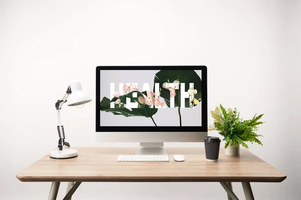 Computador com folhas verdes e saúde lettering no monitor na mesa de madeira — Fotografia de Stock