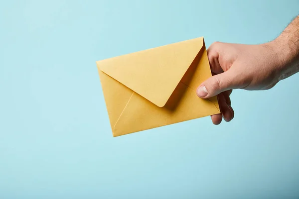 Cropped view of man holding bright and yellow envelope on blue background — Stock Photo