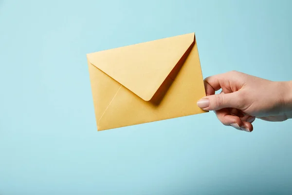 Cropped view of woman holding bright and yellow envelope on blue background — Stock Photo