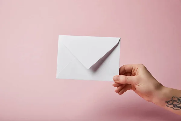 Partial view of woman with tattoo holding white envelope on pink background — Stock Photo