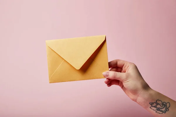 Partial view of woman with tattoo holding yellow envelope on pink background — Stock Photo