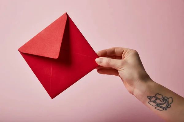Partial view of woman with tattoo holding red envelope on pink background — Stock Photo