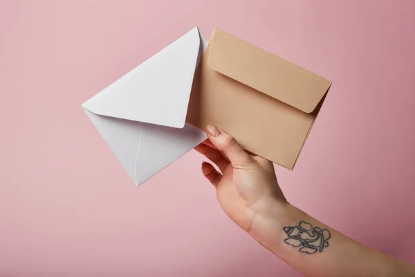 Partial view of woman with tattoo holding white and beige envelopes on pink background — Stock Photo