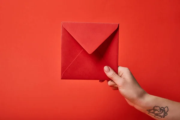 Частичный вид женщины с татуировкой, держащей красный конверт на красном фоне — стоковое фото