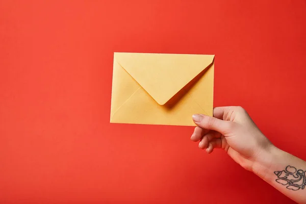 Partial view of woman with tattoo holding yellow envelope on red background — Stock Photo