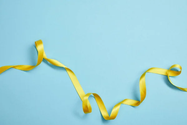 Vue du dessus du ruban de satin jaune sur fond bleu — Photo de stock