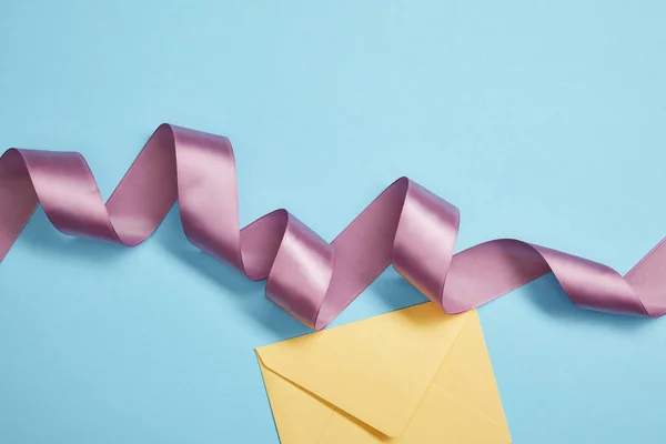 Top view of violet satin ribbon and yellow envelope on blue — Stock Photo