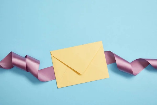 Top view of yellow envelope and violet satin ribbon on blue — Stock Photo