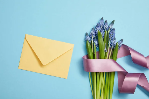 Vista superior do envelope amarelo, e jacintos azuis cobertos com fita de cetim violeta no azul — Fotografia de Stock