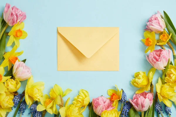 Top view of pink tulips, yellow narcissus, blue hyacinths, and yellow envelope on blue — Stock Photo