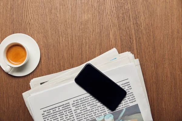 Vue du haut du journal près de tasse avec café et smartphone avec écran blanc — Photo de stock