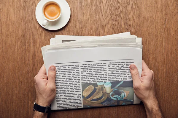 Cropped view of man holding newspaper near cup of coffee — Stock Photo