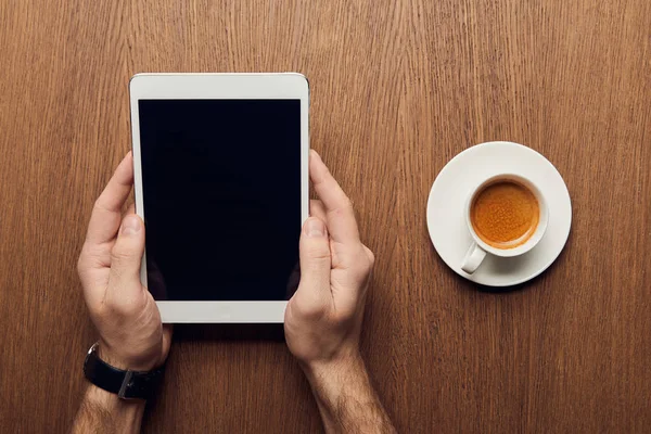 Vista recortada del hombre sosteniendo tableta digital con pantalla en blanco cerca de la taza de café - foto de stock