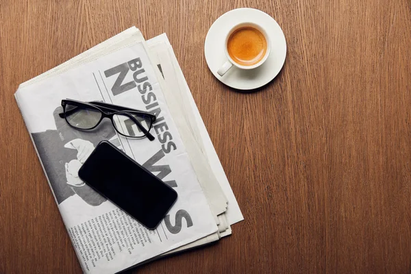 Vue du haut du journal près de la tasse avec café, smartphone avec écran vierge et lunettes — Photo de stock