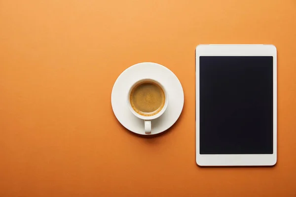 Вид сверху на цифровой планшет с пустым экраном рядом с чашкой кофе на оранжевом — стоковое фото