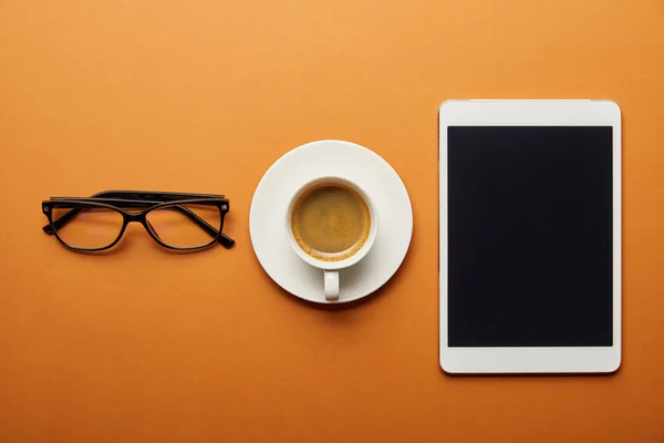 Вид сверху на цифровой планшет с пустым экраном рядом с чашкой с напитком и стаканами на оранжевом — стоковое фото