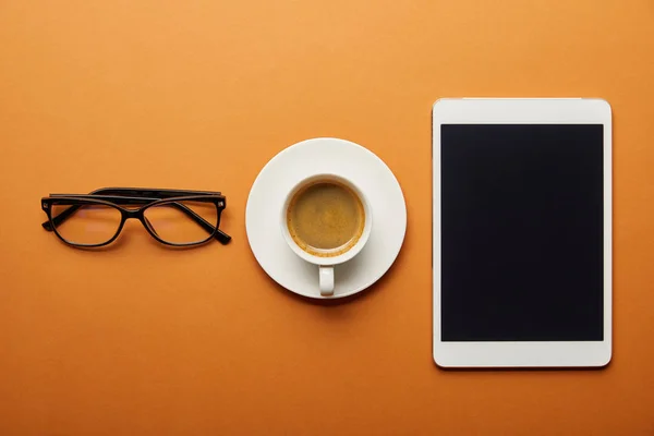 Vista superior de la tableta digital con pantalla en blanco cerca de la taza con bebida y vasos en naranja - foto de stock