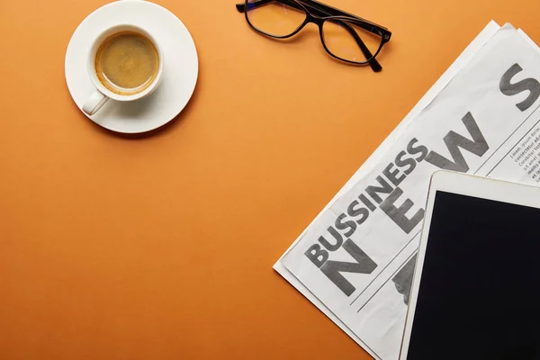 Vista superior de la tableta digital con pantalla en blanco, vasos y periódico de negocios cerca de la taza de café en naranja - foto de stock