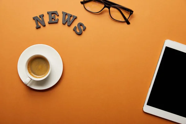 Top view of digital tablet with blank screen near glasses, news lettering and cup of coffee on orange — Stock Photo