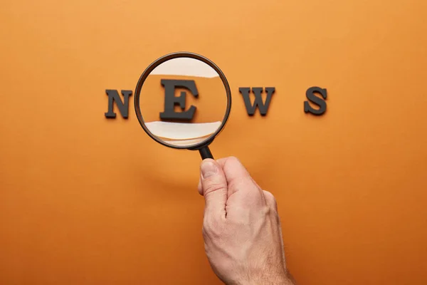 Cropped view of man holding magnifying glass and zooming news lettering on orange — Stock Photo