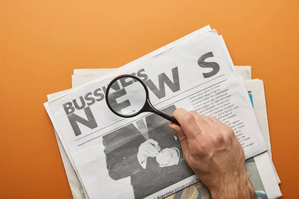 Man holding magnifying glass and zooming news lettering while reading  business newspapers on orange — Stock Photo
