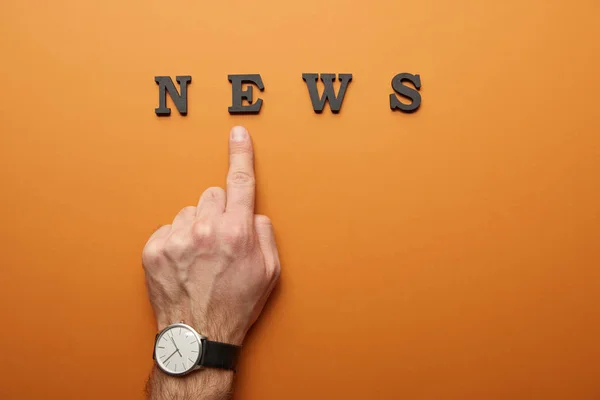 Ausgeschnittene Ansicht eines Mannes, der mit dem Finger auf einen orangefarbenen Nachrichtenaufdruck zeigt — Stockfoto