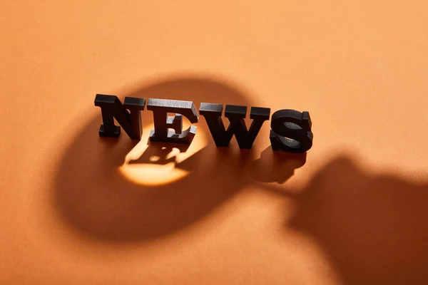 Black news lettering with copy space near shadows on orange — Stock Photo