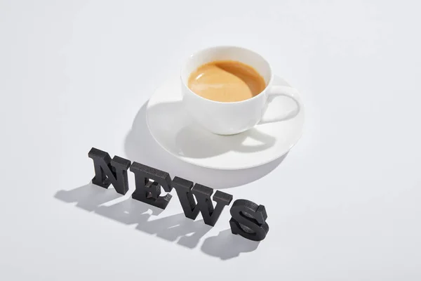 Чорні новини, що напиваються біля чашки з напоєм на білому — стокове фото