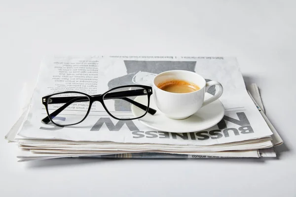 Стаканы возле чашки кофе и деловой газеты на белом — стоковое фото