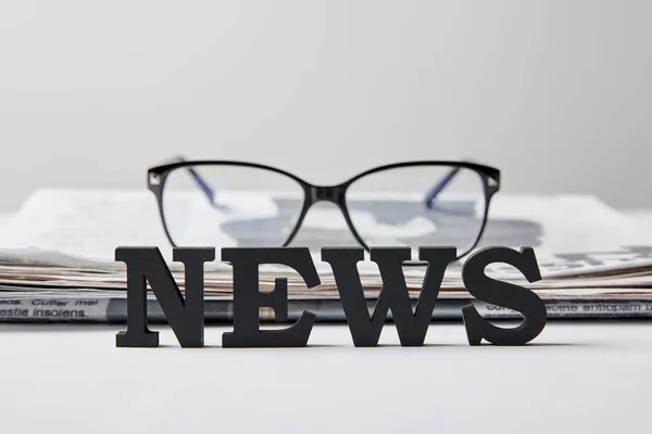Selective focus of news lettering near glasses and newspaper on white — Stock Photo