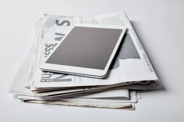 Tableta digital con pantalla en blanco cerca de periódicos de negocios con artículos en blanco - foto de stock