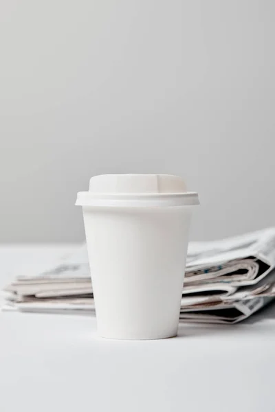 Selective focus of paper cup near newspapers on grey — Stock Photo