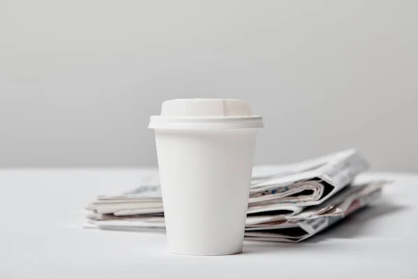 Selective focus of paper cup with drink near newspapers on grey — Stock Photo