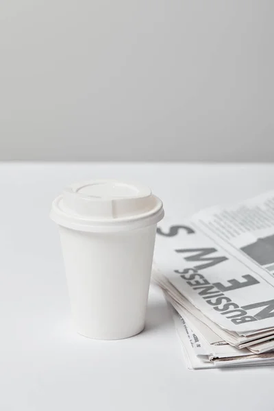 Selective focus of paper cup near business newspapers on grey — Stock Photo