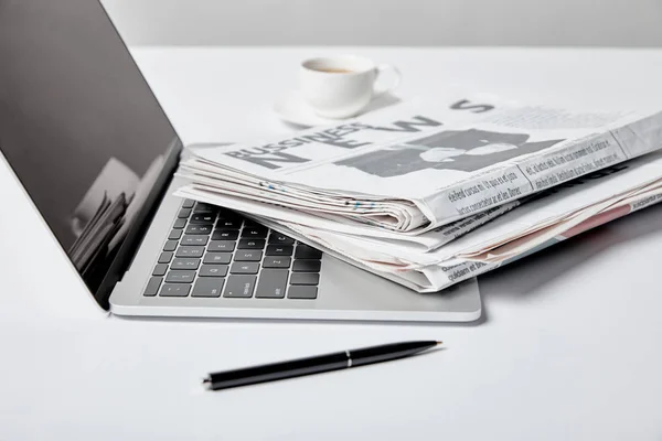 Foyer sélectif de l'ordinateur portable avec écran blanc près des journaux d'affaires, stylo et tasse — Photo de stock