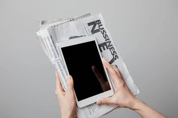 Vista recortada de la mujer sosteniendo tableta digital con pantalla en blanco y periódicos de negocios aislados en gris - foto de stock