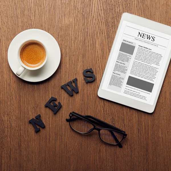 Vista superior de la tableta digital cerca de letras de noticias, vasos y taza de café - foto de stock