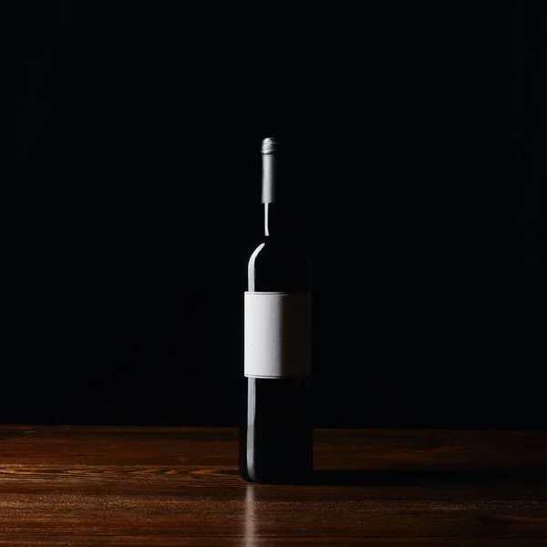Garrafa de vinho com etiqueta em branco na superfície de madeira isolada em preto — Fotografia de Stock