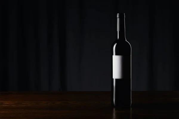 Botella de vino con etiqueta en blanco en la superficie de madera en oscuro — Stock Photo