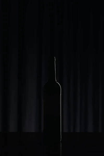 Silhouette einer Weinflasche auf schwarzer Oberfläche in der Dunkelheit — Stockfoto