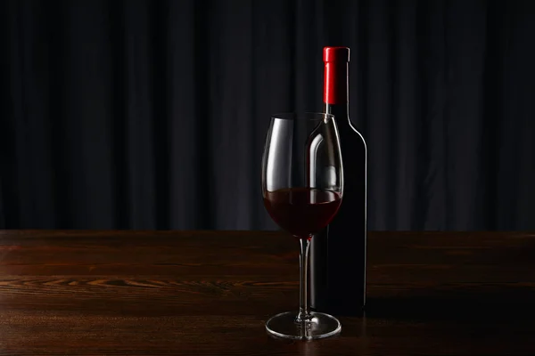 Botella de vino y copa con vino tinto en superficie de madera - foto de stock