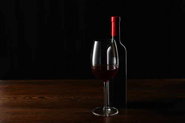 Bottle and glass of red wine on wooden surface isolated on black — Stock Photo