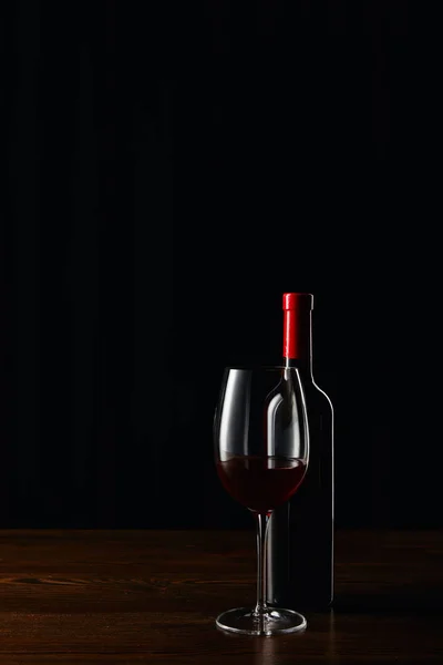 Bouteille et verre de vin rouge sur la surface en bois isolé sur noir — Photo de stock