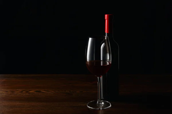 Bottle and glass of red wine on wooden surface isolated on black — Stock Photo