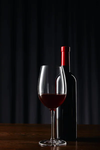 Bottle and glass of red wine on wooden surface on dark — Stock Photo