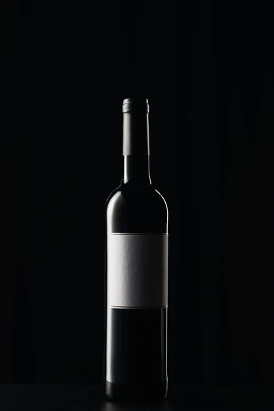 Botella de vino con etiqueta en blanco sobre superficie oscura aislada sobre negro - foto de stock