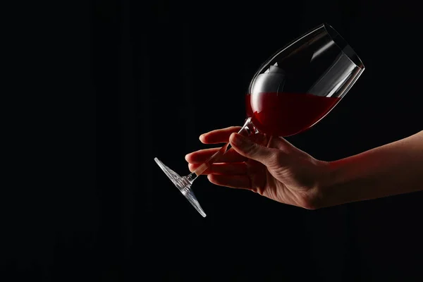 Vista parcial de la mujer sosteniendo copa de vino con vino tinto aislado en negro - foto de stock