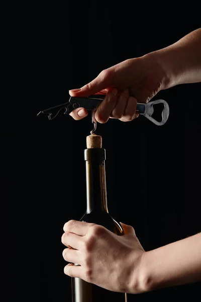 Vista recortada de niña abriendo botella de vino con sacacorchos aislados en negro - foto de stock